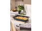 Plat de cuisson avec gratin de pommes de terre sur le comptoir de cuisine avec ustensiles et épices.