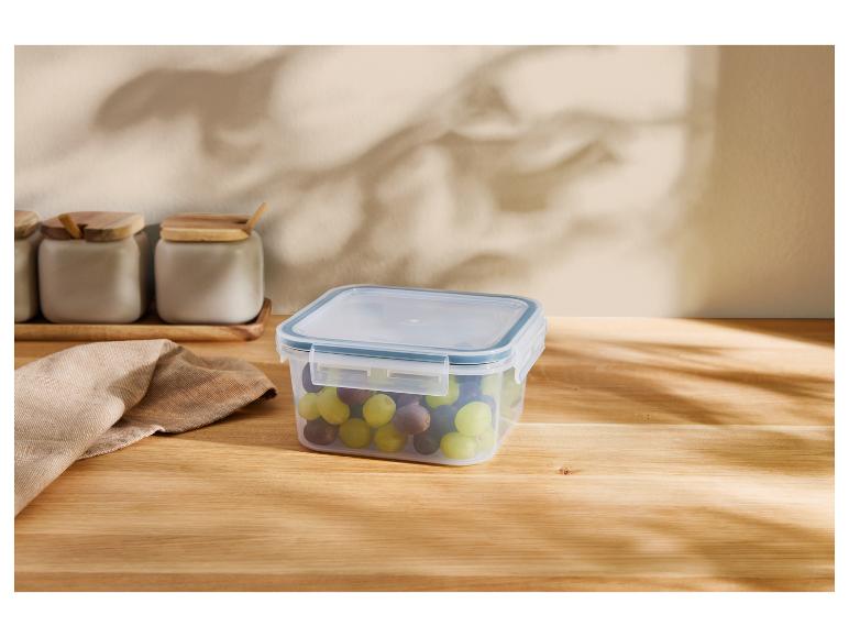 Récipient transparent avec des raisins sur une table en bois, pots en arrière-plan.