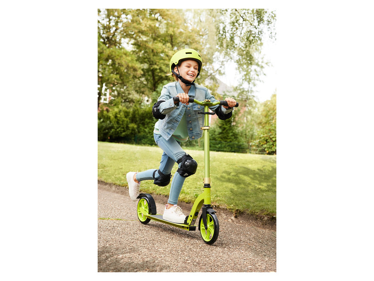 Une fille roule en trottinette verte avec un casque.