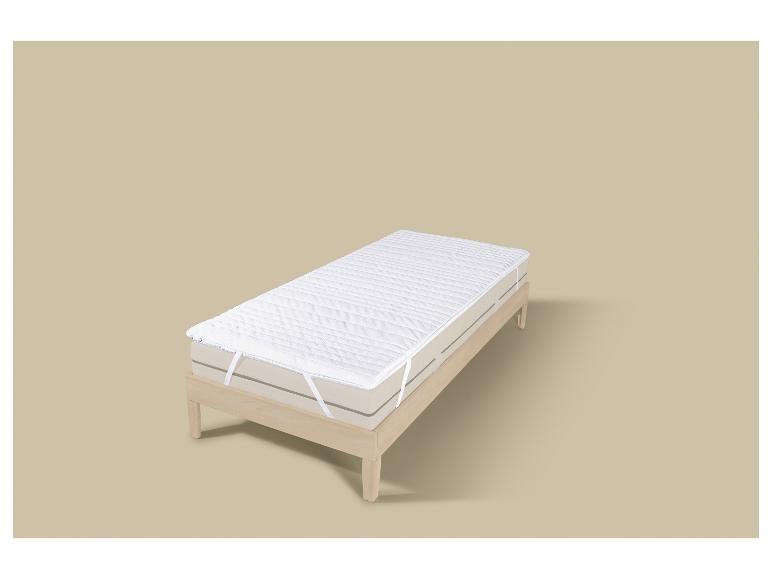 Surmatelas blanc matelassé sur un cadre de lit en bois clair.