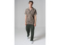 Homme portant une chemise beige à imprimé et un pantalon vert.