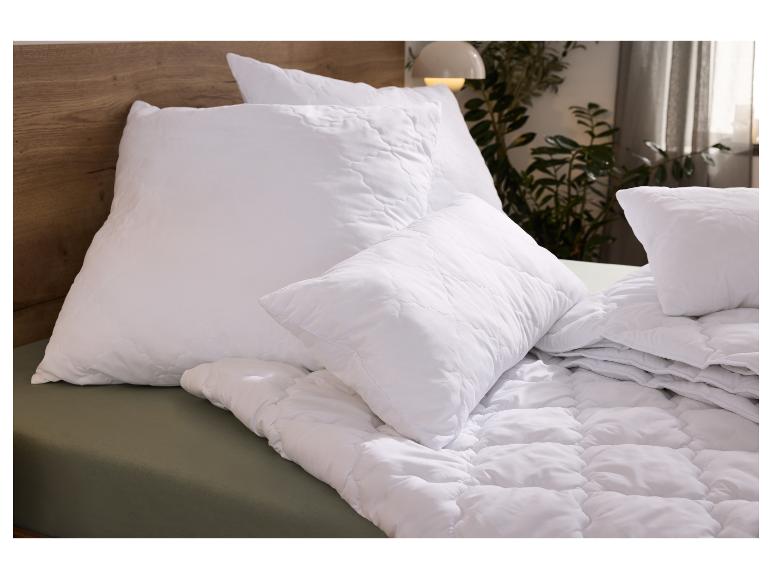 Oreiller et couette matelassés blancs sur un lit avec tête de lit en bois et drap vert.