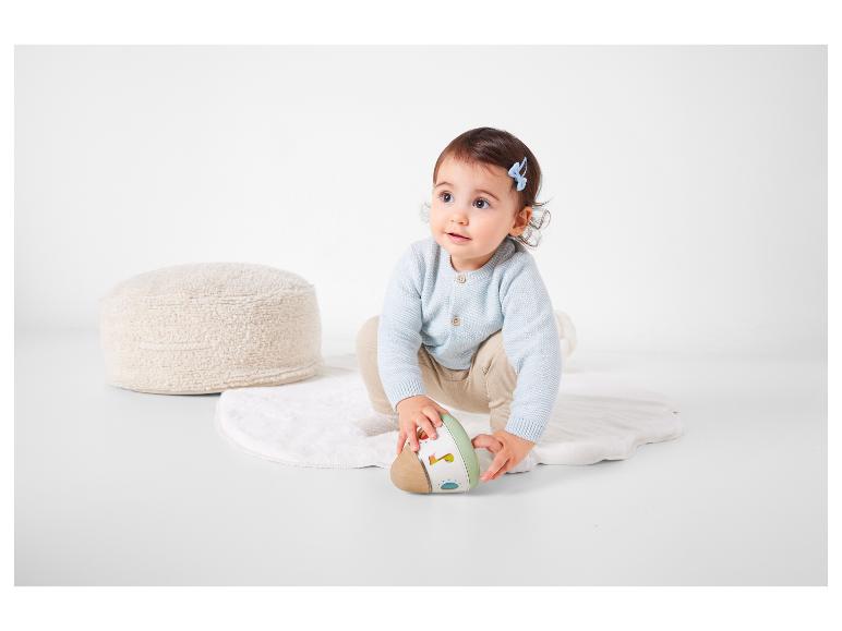 Un bébé assis sur un tapis blanc jouant avec un hochet en bois.