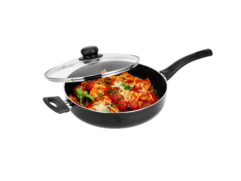 Poêle noire avec couvercle en verre, garnie de raviolis, tomates cerises et basilic