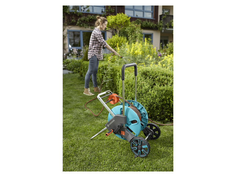 Arroseur et tuyau Gardena sur un chariot, dans un jardin.