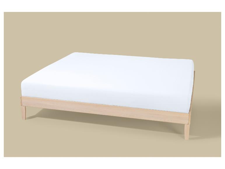 Cadre de lit en bois clair avec matelas blanc sur fond beige.