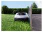 Tondeuse robot sur l'herbe à côté d'un chemin et d'une haie.