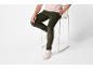 Homme en t-shirt rose clair et pantalon en velours côtelé vert foncé assis sur un tabouret blanc.