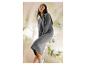 Femme en robe pull grise et baskets blanches, assise sur un fond clair avec des plantes.