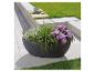 Grand pot de jardin gris foncé avec des fleurs violettes et des herbes.