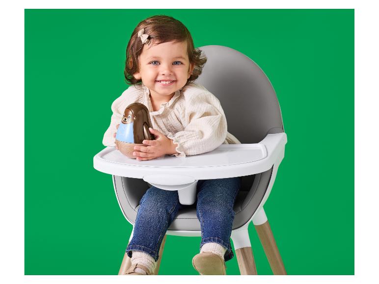 Bébé souriant dans une chaise haute tenant un hochet.
