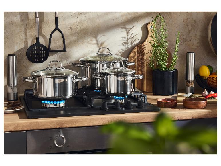 Trois casseroles en acier inoxydable sur une cuisinière à gaz, avec ustensiles de cuisine et herbes