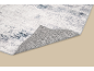 Gros plan d'un tapis blanc et gris à motifs abstraits avec un coin replié.