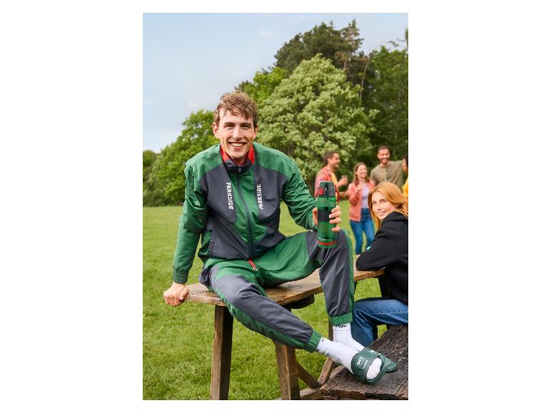 Homme souriant portant une veste verte et grise PARKSIDE® assis à l'extérieur.