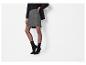 Femme en jupe grise, haut noir, blazer noir, collants noirs et bottines noires.