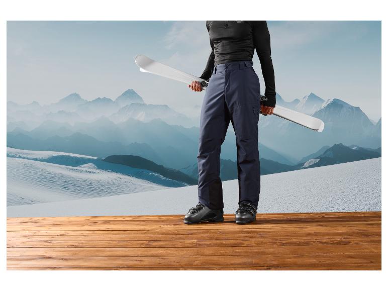 Skis, chaussures de ski et pantalon sur fond de paysage de montagne.