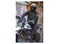 Un motard avec un casque et une veste noire sur une Ducati Scrambler blanche.