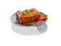 Une assiette avec des lasagnes, des tomates et du basilic, à côté d'un disque pour hachoir à viande.