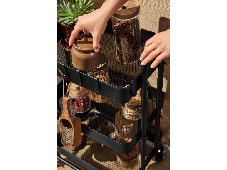 Chariot de cuisine noir avec des bocaux de café, d'épices et une plante.