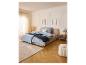 Chambre avec lit, table de chevet LIVARNO®, tapis et pouf aux couleurs claires.