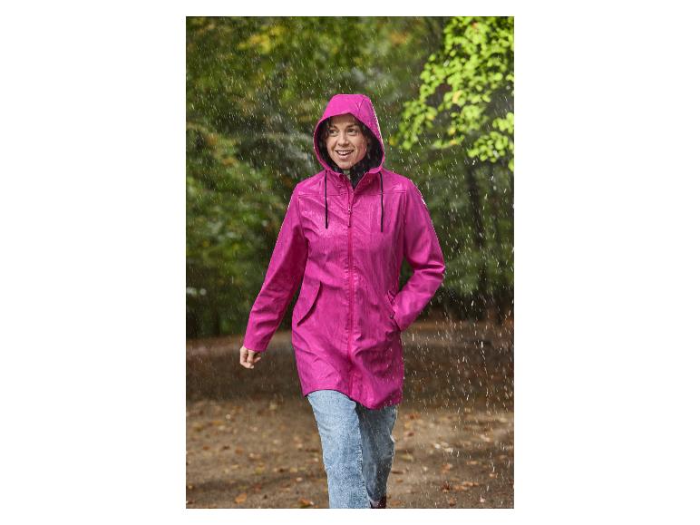 Une femme en imperméable rose pour femme CRIVIT marche sous la pluie.