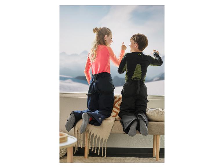 Deux enfants en tenue de ski regardant par une fenêtre des montagnes enneigées.