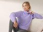 Une femme portant un pull violet à col roulé et un legging gris.