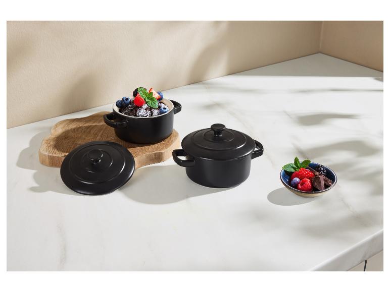 Casseroles en céramique noires avec fruits et chocolat sur une surface en marbre clair.