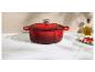 Cocotte en fonte émaillée rouge avec couvercle, huile d'olive et piments rouges sur un comptoir en marbre.