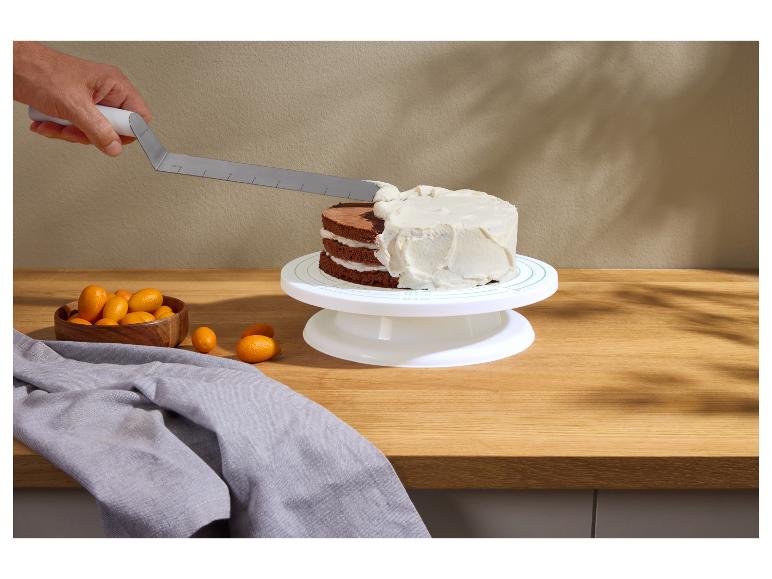Main glaçant un gâteau au chocolat sur un plateau tournant, avec des kumquats et un torchon gris.