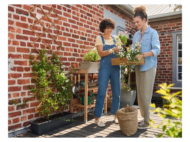 Deux femmes plantent des fleurs dans une jardinière sur une terrasse en bois.