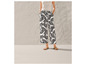 Une femme porte un pantalon blanc avec un motif de feuilles noires et des sandales beiges.