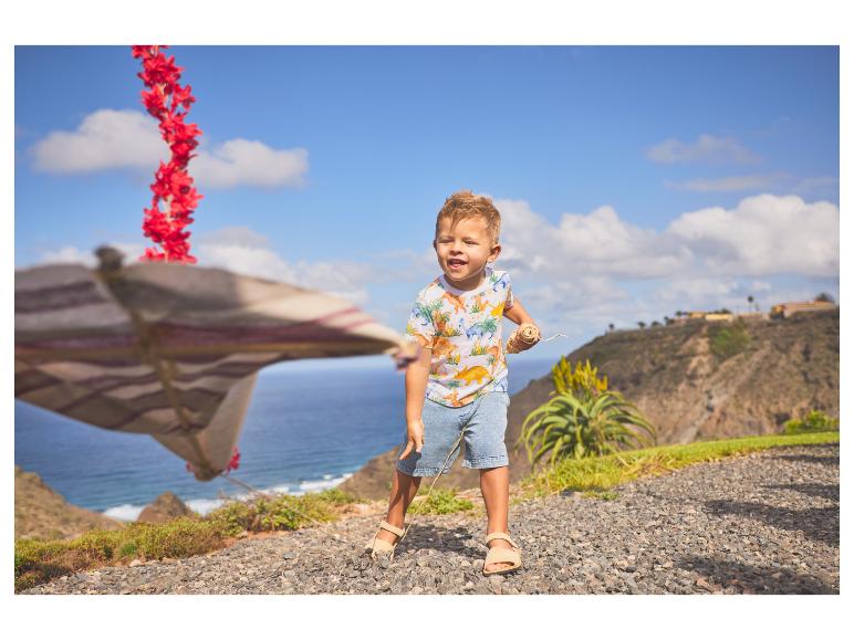 Garçon en t-shirt dinosaure et short jouant au bord de la mer.