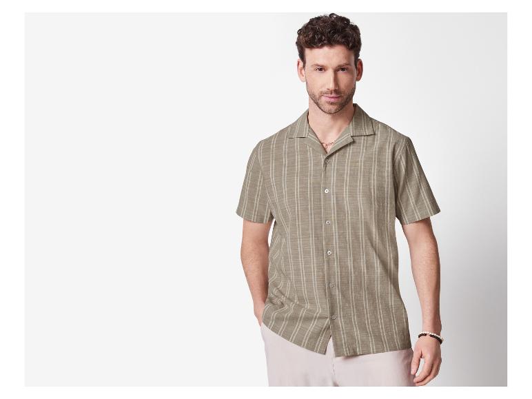 Homme en chemise à manches courtes rayée beige et pantalon clair.