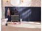 Salle de bain avec meuble vasque bleu foncé, lavabo noir, miroir rond et papier peint floral.