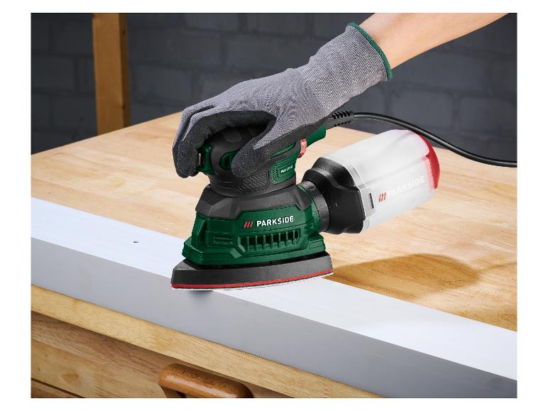 Main gantée ponçant une planche blanche avec une ponceuse Parkside sur une table en bois.