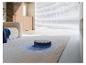 Aspirateur robot sur un tapis dans un salon lumineux avec un canapé et des fenêtres.