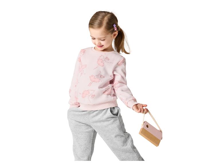 Petite fille en sweat rose à motifs ballerines et pantalon de jogging gris, tenant un sac en bois.