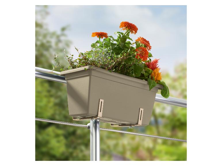 Jardinière de balcon grise avec des fleurs oranges et vertes, fixée à une balustrade métallique.