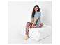 Une femme assise sur un pouf blanc avec un t-shirt bleu et un pantalon à imprimé paisley.