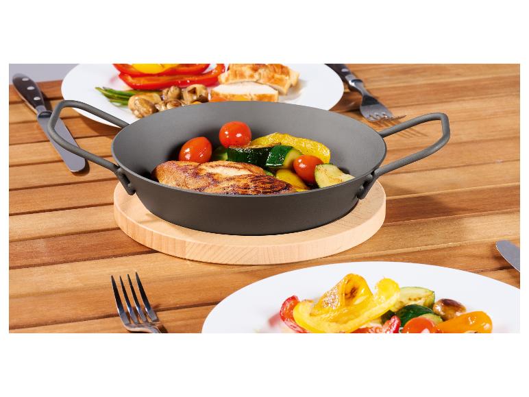 Poulet grillé et légumes dans une poêle à deux poignées sur une planche en bois.