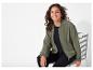 Une femme porte une veste bomber verte et un pantalon noir.
