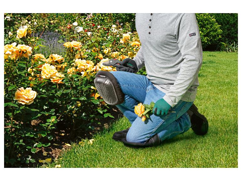 Jardinier agenouillé, avec genouillères et gants, taillant des roses jaunes.