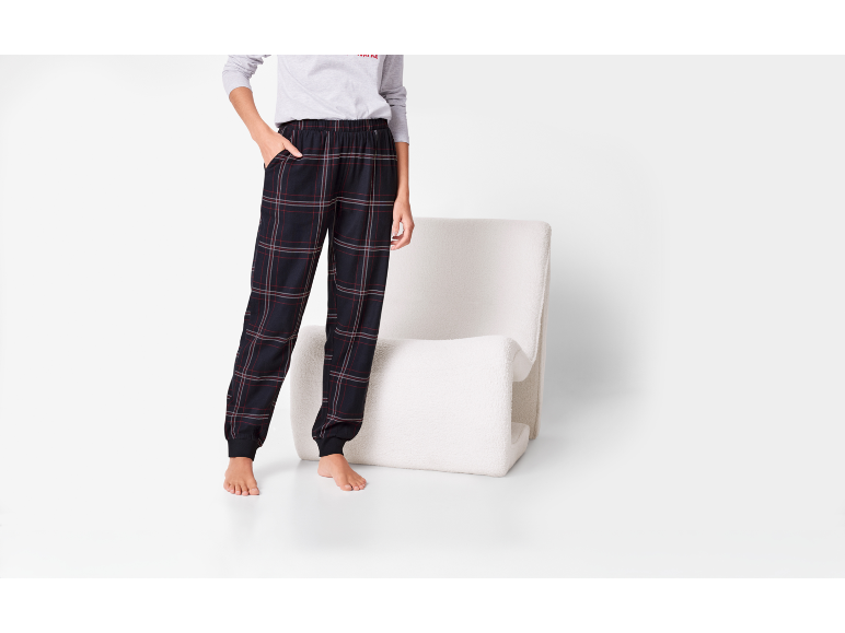 Pantalon de pyjama à carreaux foncés avec t-shirt gris et poignets, à côté d'un fauteuil blanc.