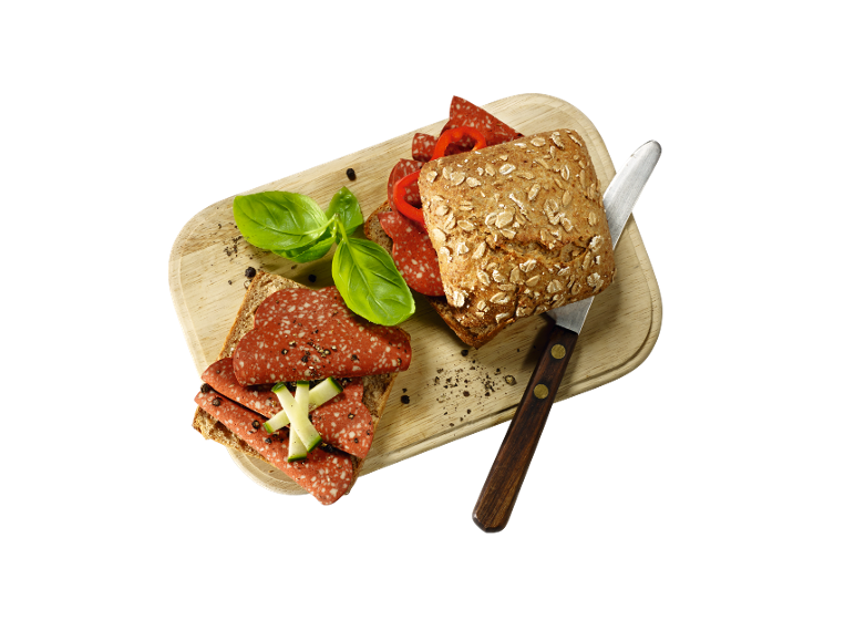 Sandwichs de pain complet avec salami, poivron, basilic et concombre sur une planche en bois.