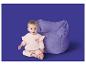 Bébé en survêtement rose à cœurs, assis à côté d'un pouf violet.