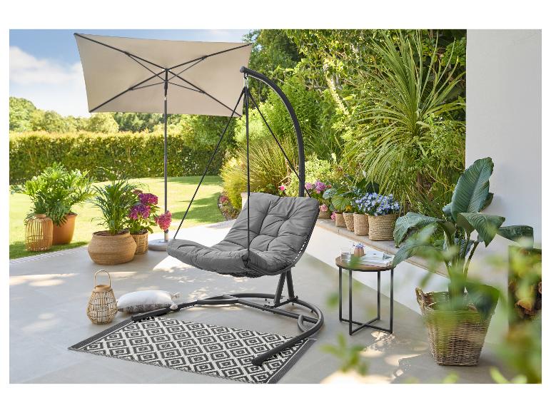 Fauteuil suspendu gris avec coussin, parasol et plantes sur une terrasse.