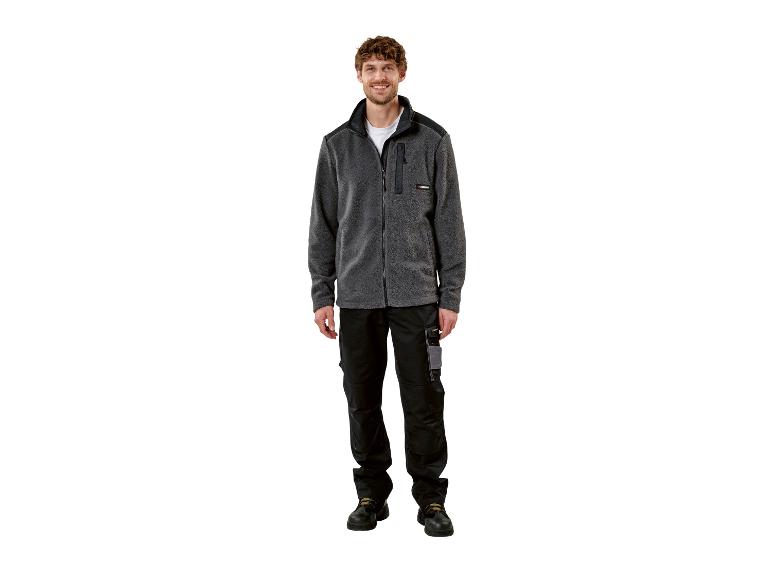 Homme souriant en veste polaire grise et pantalon de travail noir.