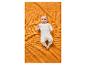 Bébé en grenouillère blanche à étoiles, allongé sur une couverture gaufrée orange.