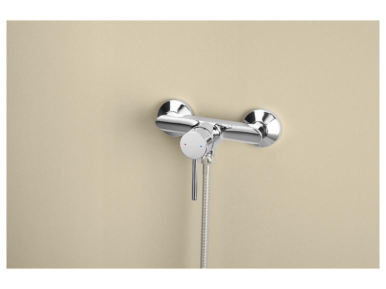Mitigeur de douche chromé avec thermostat et flexible sur un mur beige.